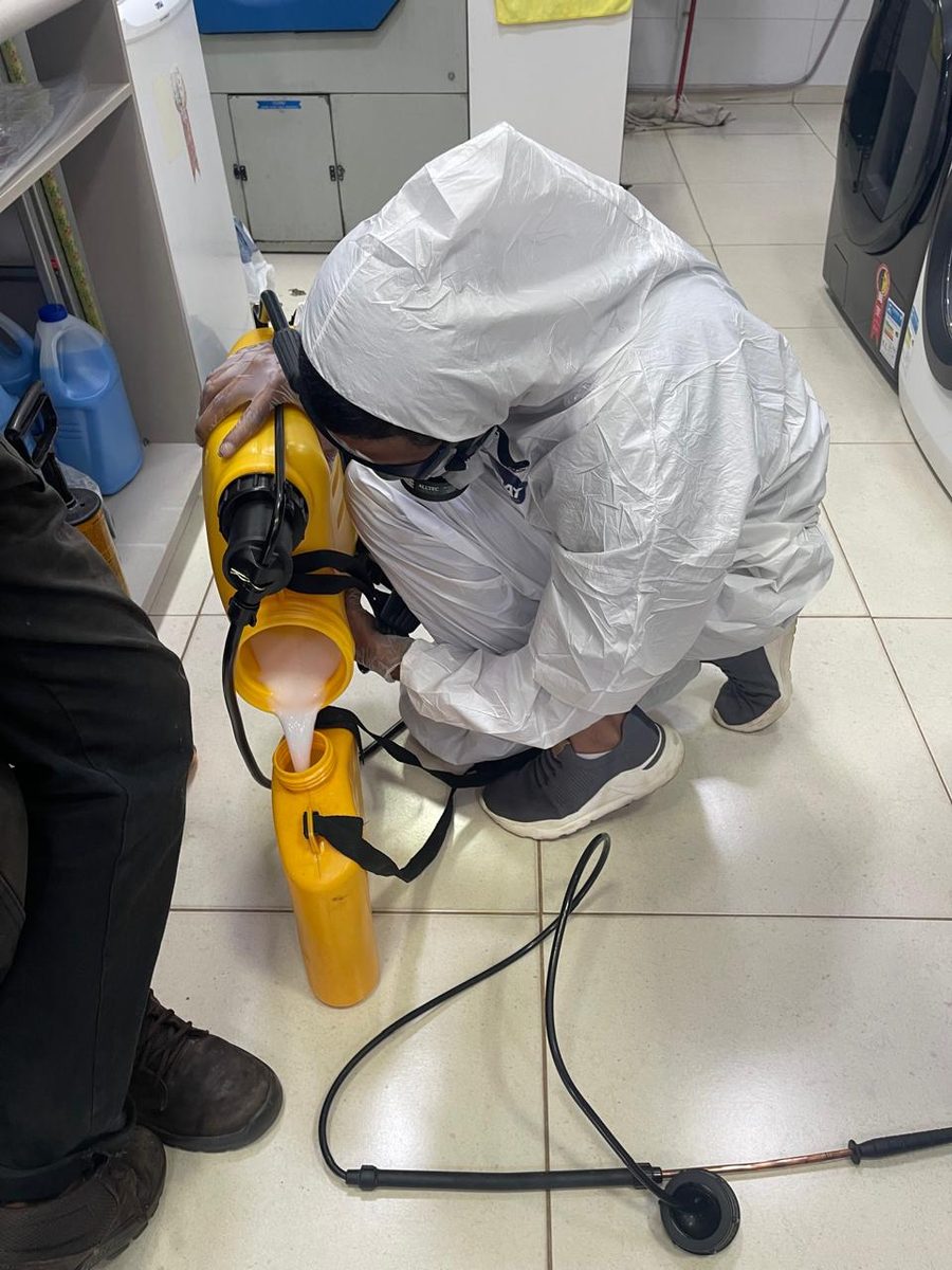 Técnico da DDTizaMax preparando o produto no pulverizador, de macacão, óculos e luvas